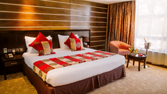 Superior Double Room at Boma Inn Eldoret featuring a double size bed, a sofa chair with centre table, bedside table on either side, and a window with curtain.