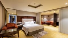 A room at Citadel Sarovar Portico, Bangalore featuring double size bed, a sofa chair on one side and a seating area on the other side.