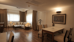 A large living and dining area with wooden flooring, a dining table, upholstered chairs, and wide windows allowing ample natural light in the Executive Suite at Clarks Amer, Jaipur.