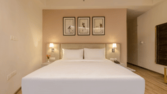 A double bed with neat linens set against a beige wall with 3 framed art pieces at Golden Tulip - Sector 80, Gurugram.
