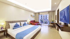 A hotel room with a balcony featuring a king size bed, a flat screen television, and ambient lighting - Golden Tulip, Candolim, Goa