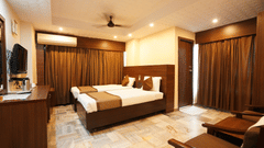 Deluxe room interior with a comfortable bed, wooden furnishings and warm lighting at Hotel Jaya Residency, Kakinada.