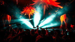 A vibrant nightclub scene with a crowd of people dancing under large, spiky, orange and red decorative lights. Bright beams of light cut through the smoky atmosphere, creating an intense, energetic vibe.