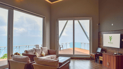 Indoor lounge with a cosy sofa set, large windows, and a view of hills and sky through glass doors at Ibex Resorts, Coonoor (Tapas).