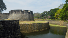 Palakkad Fort, one of the popular tourist places in Palakkad, beside calm water, surrounded by greenery under a bright sky, showcasing traditional architecture and peaceful surroundings