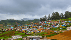 A colourful hillside village with patchwork fields under a gloomy sky