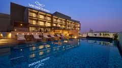 A modern hotel building is illuminated at dusk, featuring a rooftop swimming pool reflecting the hotel's signage and nearby lounge chairs. - Iris Sarovar Portico, Sector 85, Gurugram