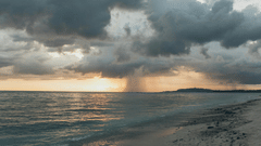 Rain falling over the ocean with the sun setting on the horizon, creating a moody scene.