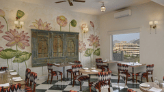 A brightly lit restaurant interior with a black and white checkered floor, floral-themed wall art, and dark wood furniture at Khas Mahal Suites, Udaipur.