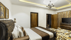The spacious presidential suite bedroom with a king size bed, upholstered headboard, bedside tables, chandelier lighting, television unit and patterned flooring at La Marvella, Bengaluru.