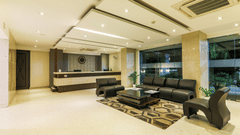Lobby area of Magnus Star Residency, Koregaon Park Annexe, featuring a modern reception desk, black leather seating, glass walls with views of greenery, geometric rug, and warm recessed ceiling lighting.