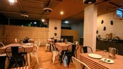 Restaurant at Magnus Vosiv Suites, Kalyani Nagar featuring several sets of tables and chairs and a shelf where food utensils are kept.