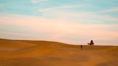 Neemrana Tijara Fort Palace - A man holding a camel and walking on a desert