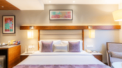 A bedroom at Nirvana Sarovar Portico, Gorakhpur featuring a king size bed, wall lamps, framed artwork, and a side table.  