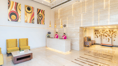 The front desk reception at Nirvana Sarovar Portico, Gorakhpur featuring staff members, seating area, abstract wall art, and luggage cart.