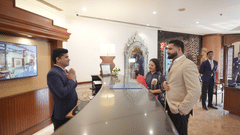 Hotel staff members interacting with guests at the lobby of Park Plaza Ludhiana featuring marble flooring wooden wall panels decorative archway and a digital display screen.