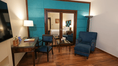 A sitting area at Park Plaza Ludhiana featuring two blue armchairs a wooden table teal accent wall large mirror warm wall lamps and a wall-mounted TV.