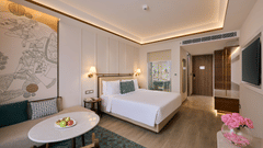 Deluxe King Room at Prachi Sarovar Premiere, Bhubaneswar, with a large bed, an entrance door, a sofa, and an oval coffee table with a plate.