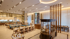Flavours dining hall at Prachi Sarovar Premiere, Bhubaneswar, with long wooden tables, chairs, a decorative food cart, and ceiling lights.