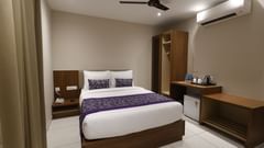 A deluxe room at Pride Biznotel Canopus Digha featuring a bed, bedside table on either side, air conditioner, fan, a cabinet table where tea and coffee maker is kept
