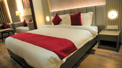 Suite room with large bed and red linens at Pride Biznotel Haldwani featuring a sitting space in the background