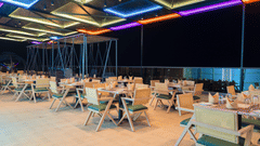 An outdoor dining area with multiple tables and chairs, illuminated by colourful strip lighting on the overhead canopy at night | Pride Elite Chhatrapati Sambhajinagar