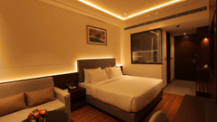 A room at Pride Elite Haridwar featuring king size bed with comfortable sofas. The room is lit with ceiling lights and lights around the bed and sofa.
