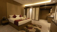 A spacious hotel room at Pride Resort, Jodhpur, featuring a neatly made bed with decorative cushions and towel art.