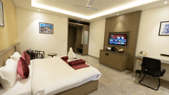 A modern hotel room at Pride Resort, Jodhpur, with a large bed, desk, TV, and warm ceiling lighting.