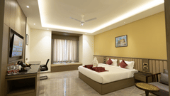 A spacious hotel room at Pride Resort, Jodhpur, featuring a large bed, seating area, desk, and soft ceiling lighting.