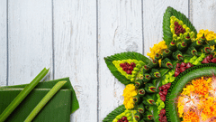 Floral rangoli design arranged on the floor with green leaves, flowers, and decorative patterns visible.