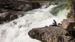 a person sitting on a rock beside a massive waterfall