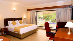 Hill View Room featuring a floor to ceiling window, a double bed, and desk and a chair inside Raj Park, one of the top hotels in Tirupati