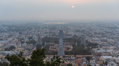 An aerial view of the town of tirupati with numerous temple's gopuram in view and other buildings and trees also in view with the sun setting in the background.