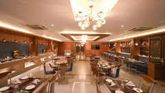 Elegant restaurant dining hall at Rivera Sarovar Portico, Ahmedabad featuring neatly arranged dining tables, decorative chandeliers and contemporary interiors.