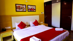 A romantically decorated hotel bed with white linens, a red runner, red accent pillows, and swan towel art surrounded by flower petals.