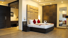 A luxury hotel room featuring a large bed with a tall, padded beige headboard, white linens, and two red accent pillows.