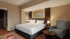 Spacious bedroom at Royal Tulip, Kathmandu, with a large bed and a cosy armchair, perfect for relaxing.