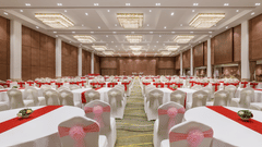 A large banquet hall set up with numerous round tables, white tablecloths, and red runners at Royal Tulip, Kathmandu.