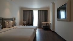A spacious hotel room with twin beds, a sitting area with a sofa and chairs, and a television on the wall | Deluxe Twin Bed Room | Sarovar Portico, Hanumangarh