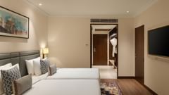 A bedroom at Sarovar Portico, Hanumangarh, with two single beds, a television, and a doorway.