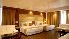Spacious room at Sarovar Portico, Somnath with multiple beds, seating area, curtains, and a patterned headboard wall.