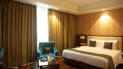 Room at Sarovar Portico, Somnath featuring a bed, chairs, table, and floor-to-ceiling curtains.