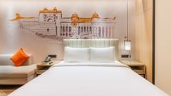 A room at Sarovar Premiere Alwar with a bed, a bedside table, and a mural of a building on the wall.