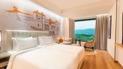A twin bed hotel room at Sarovar Premiere Alwar with a view, a seating area, and a wall mural of a building.