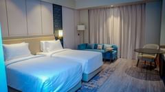 A hotel room in Hargeisa, featuring twin beds, a couch, a work desk, and warm lighting - Serene Sarovar Premiere Hargeisa