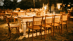 An outdoor dining area set up for an event with wooden tables and chairs under warm string lights.