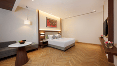 Skywings Sarovar Portico Mathura suite room with king bed, herringbone wood flooring, work desk, framed wall art, and bright natural lighting.