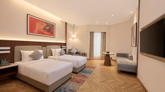 Skywings Sarovar Portico Mathura standard twin room with two single beds, colorful patterned rug, herringbone wood flooring, and warm ambient lighting.
