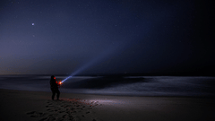 A person holding a flashlight switched on roaming around the beach during the night.